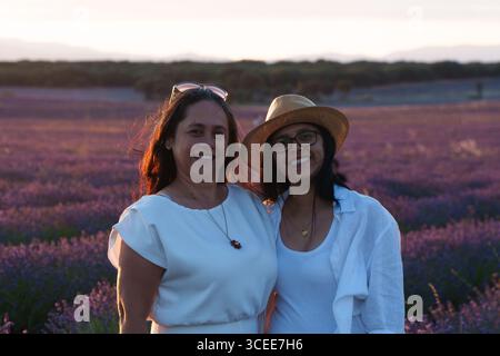 Due donne sono in piedi in un campo di lavanda. Uno di loro indossa un cappello di paglia Foto Stock