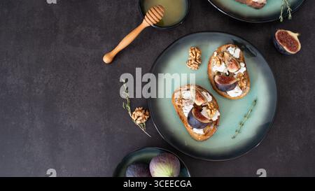 Vista dall'alto di due toast al formaggio di fico e capra con cucchiaio di miele, ciotola di miele e fichi su sfondo nero con spazio per copiare Foto Stock