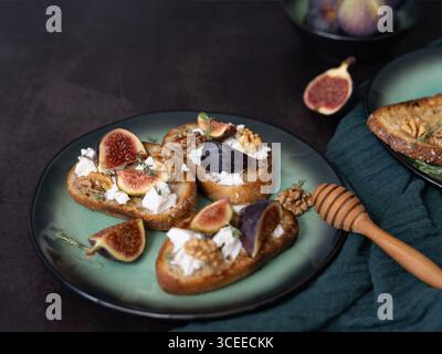 Tre brindisi con fichi e formaggio di capra su piatto verde con miele, noci, timo, asciugamano da cucina verde, vista frontale, copia spazio Foto Stock