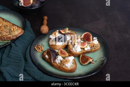 Vista frontale orizzontale di tre toast di fichi e capra su piatto verde con miele, noci, timo, asciugamano da cucina verde e spazio per copiare Foto Stock