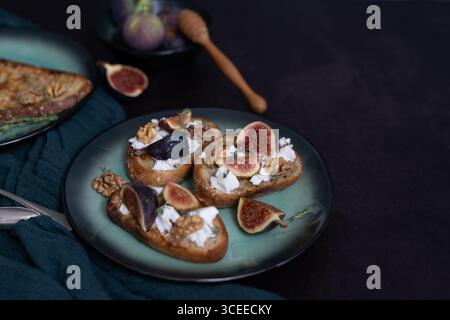 Vista frontale orizzontale di tre toast di fichi e capra su piatto verde con miele, noci, timo, asciugamano da cucina verde, spazio per copiare Foto Stock