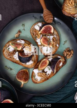 Vista dall'alto di tre toast di formaggio di fico e capra su un piatto verde con miele, noci, timo, cucchiaio di miele e asciugamano da cucina verde Foto Stock