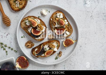 Vista dall'alto primo piano orizzontale di tre toast di fichi e capra con timo, fichi sul piatto laterale, sfondo grigio, saporito mix dolce Foto Stock