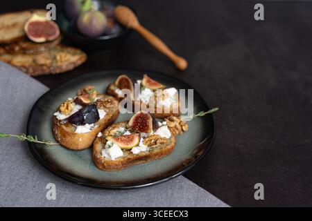 Vista frontale orizzontale di tre toast di formaggio di fico e capra su piatto verde con miele, noci, timo, saporito mix dolce, sfondo scuro Foto Stock