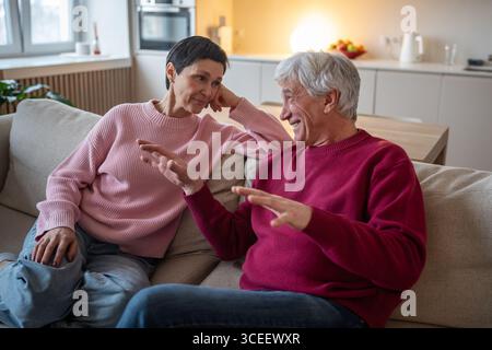 Un pensionato che racconta storie a una moglie tenera. Conversazione felice a casa, ascolto impegnato sul divano Foto Stock