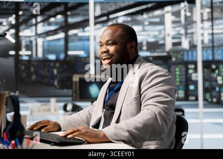 Allegro sviluppatore di software nel data center che controlla lo stato dell'infrastruttura e mostra indicatori di prestazioni stabili. Il dipendente della sala server è soddisfatto dopo aver completato correttamente le operazioni Foto Stock