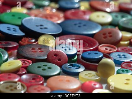 primo piano di una pila di bottoni colorati da cucire di varie dimensioni, sfumature e motivi. Bottoni rotondi in plastica multicolore, sfondo artigianale, Foto Stock