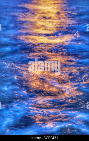 Luce dorata del sole che tramonta, emettendo un caldo bagliore sull'acqua blu fredda e dinamica Foto Stock