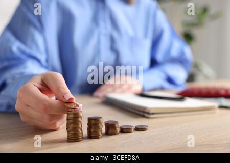 Donna impilando monete a tavola di legno, primo piano Foto Stock
