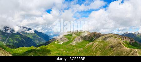 Vista mozzafiato delle montagne Panorama delle vette alpine e dei lussureggianti prati sotto un cielo nuvoloso Foto Stock