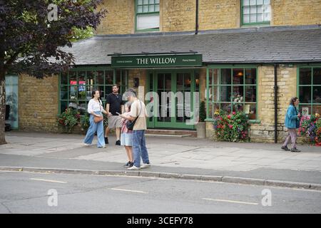 Vista sulla strada dell'esterno del pub Stone con persone in un abbigliamento informale. Bourton-on-the-Water, Inghilterra Foto Stock