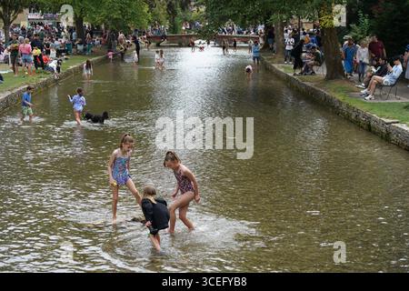 Le famiglie trascorrono una giornata divertente lungo un ruscello calmo in estate. Bourton-on-the-Water, Inghilterra Foto Stock