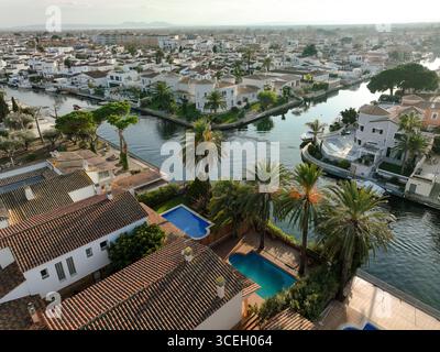 Empuriabrava, Spagna - 31 dicembre 2023: Veduta aerea dei corsi d'acqua che si snodano attraverso la città, riflettendo il cielo, con palme che gettano ombre sulle ville e sulle piscine. Foto Stock