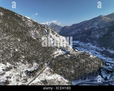Veduta aerea di edifici innevati annidati tra le montagne, il bianco intenso che contrasta con il verde intenso degli alberi, Sestriere, Piemonte, Italia. Foto Stock