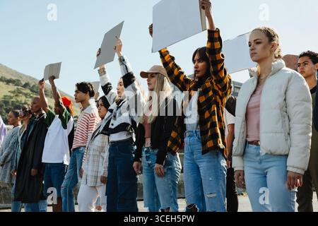 Un gruppo eterogeneo di giovani uomini e donne in piedi in solidarietà, tenendo cartelli bianchi durante una manifestazione all'aperto, promuovendo awa sociali e comunitari Foto Stock