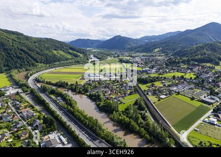 Vista panoramica aerea di Peggau, una città annidata tra le verdi montagne, con il tortuoso fiume Mur e l'autostrada S36 che attraversa il landsc Foto Stock