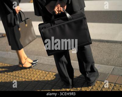 Uomini d'affari giapponesi, con le valigie, ad un incrocio nel quartiere degli affari di Tokyo, in Giappone. Rilasciato Foto Stock