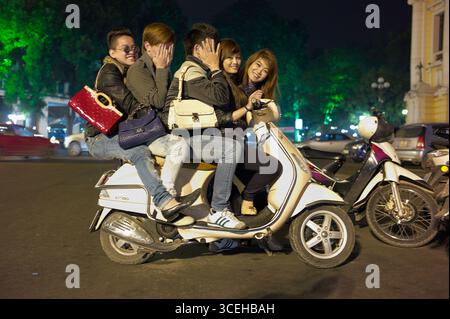 Cinque giovani adulti cram su uno scooter per le strade del Vietnam durante la notte. Foto Stock