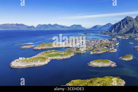 Vista aerea di Henningsvær, un gruppo di isole collegate da ponti, con edifici rossi e gialli vibranti che contrastano con il mare blu profondo, Henningsvær, Nordland, Norvegia. Foto Stock