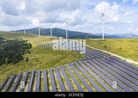 Vista aerea dei pannelli solari che si crogiolano al sole vicino alle torreggianti turbine eoliche sullo sfondo montuoso, Lachtal, Stiria, Austria. Foto Stock