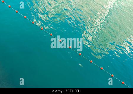 Vista minimalista dall'alto verso il basso di una barriera di corda rossa galleggiante su una superficie cristallina e scintillante di acqua di mare turchese. Foto Stock