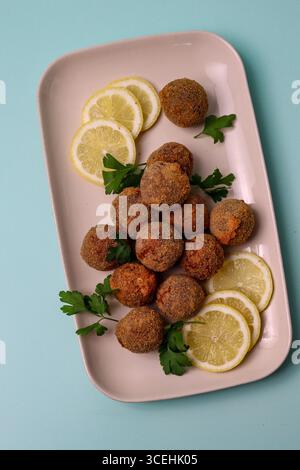 Un bicchierino piatto dall'alto di antipasti salati fritti, probabilmente polpette o crocchette, disposti su un piatto con prezzemolo fresco e fette di limone Foto Stock