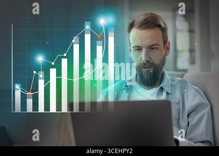 Young man analizza le tendenze finanziarie e la crescita del mercato mentre lavora su notebook in uno spazio abitativo moderno Foto Stock