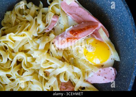 Cottura della pasta in una padella, infuso di spezie, mescola con pezzi croccanti di salsiccia fritta e un uovo fritto perfettamente cotto, creando un delizioso e h Foto Stock