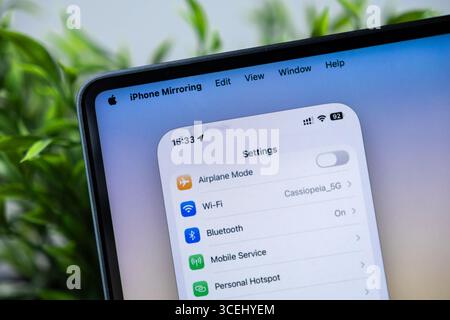Poznan, Polonia - 15 agosto 2025: L'applicazione iPhone Mirroring visualizza le impostazioni di uno smartphone su un moderno display per laptop, con tecnologia macOS 26 e. Foto Stock