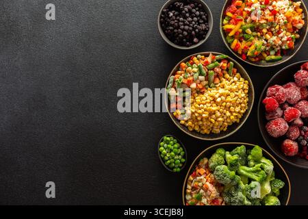 Una varietà di verdure e frutta congelate disposte in piatti, su sfondo scuro, catturando l'essenza della conservazione estiva per l'inverno Foto Stock