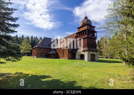 La chiesa articolare in legno di Svaty Kriz nel distretto di Liptovsky Mikulas, in Slovacchia, sorge su un prato verde sotto un cielo blu con nuvole bianche Foto Stock
