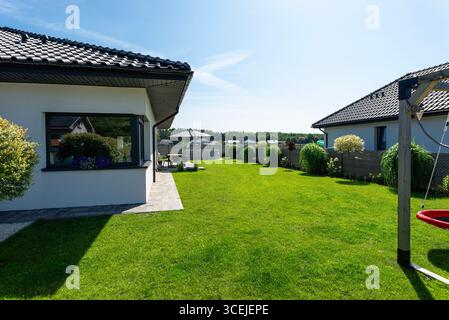 Un bellissimo giardino con erba verde, un tavolo da patio e ombrello visibili, una casa con un bel tempo estivo, un colpo molto ampio. Foto Stock