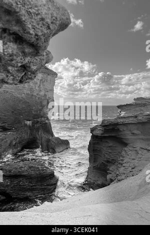 Scogliere ripide sul Mar Mediterraneo in Corsica con onde che si infrangono sulle rocce e nuvole che riempiono il cielo estivo Foto Stock