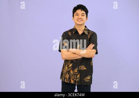 un giovane uomo che indossa un abito batik con le braccia incrociate si posa sicuro di sé Foto Stock