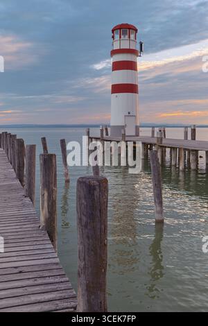 Vista dal secondo molo verso un faro bianco-rosso, pesca pastello e tramonto blu che si riflette su Neusiedler SEE, Austria. Foto Stock