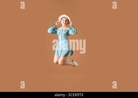 Donna con un elegante cappello che salta su sfondo marrone Foto Stock