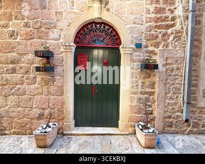 Una porta di legno verde con cassetta postale rossa e telaio ad arco in pietra su una parete rustica. Architettura, tradizione, ingresso e identità residenziale in città Foto Stock