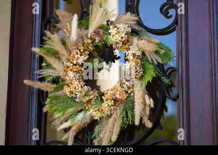 Corona autunnale fatta di ortensie essiccate, pampas erba e rami di pino appesi su una porta rustica in legno. Atmosfera di campagna e stile vintage Foto Stock