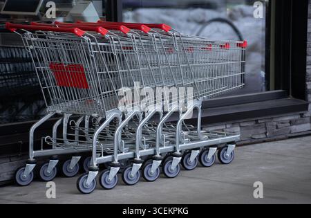 cinque carrelli vuoti insieme all'esterno del negozio di alimentari in acciaio inossidabile con ruote e maniglie rosse impilate insieme all'esterno del negozio di alimentari Foto Stock