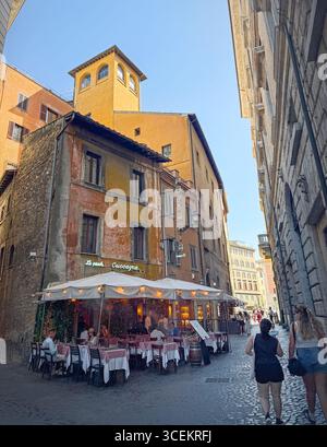 ROMA, ITALIA - 30 luglio 2025, vivace vista sul centro città e un'affascinante trattoria con tavoli adagiati su una strada acciottolata. I clienti potranno cenare all'aperto Foto Stock