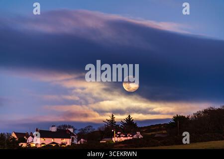 Questa splendida fotografia cattura una serena scena serale con una luna piena luminosa che si innalza sopra un paesaggio rurale. Foto Stock