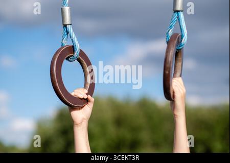 Primo piano delle mani dei bambini afferrando anelli da ginnastica all'aperto con cielo azzurro, concetto di sport, forza e gioco Foto Stock