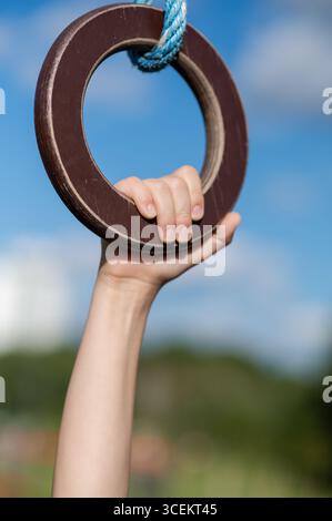Primo piano delle mani dei bambini afferrando anelli da ginnastica all'aperto con cielo azzurro, concetto di sport, forza e gioco Foto Stock