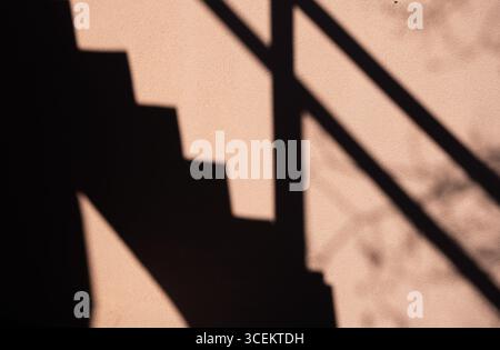 scala e ringhiera ombra su pareti esterne in cemento o cemento color pesca linee nere angoli e forme create dall'ombra esterna delle scale Foto Stock