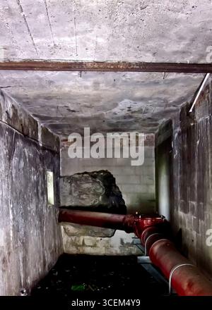 Un'immagine interna di una stanza in cemento con un tubo rosso che la attraversa. Foto Stock