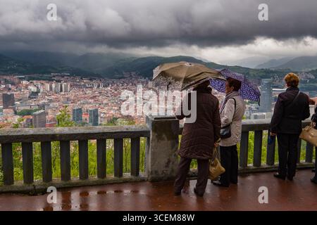 Il gruppo di donne ombrelli azienda guardando alla vista di Bilbao dal Monte Artxanda, Bilbao, Biscaglia, Paesi Baschi Foto Stock