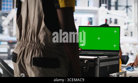 Le impostazioni del sistema di messa a punto di un esperto di impianti fotovoltaici su un PC con schermo verde. Il responsabile lavora su un laptop presso l'impianto di produzione di pannelli solari per la configurazione delle linee di assemblaggio. Telecamera A.. Foto Stock