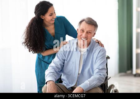 Ritratto di un uomo anziano felice con disabilità e della sua infermiera femminile a casa di riposo. Assistenza medica professionale per anziani Foto Stock