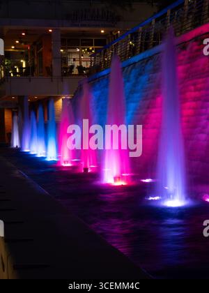 Fontane presso la Waterway Square nel Woodlands, Texas, illuminate da colori vivaci che proiettano un riflesso di luce blu, viola e rosa a poca distanza Foto Stock