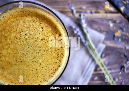 Primo piano del caffè appena preparato con schiuma cremosa, disegnato su un tavolo in legno rustico con accenti lavanda, perfetto per sfondi, marchi di caffè, e. Foto Stock